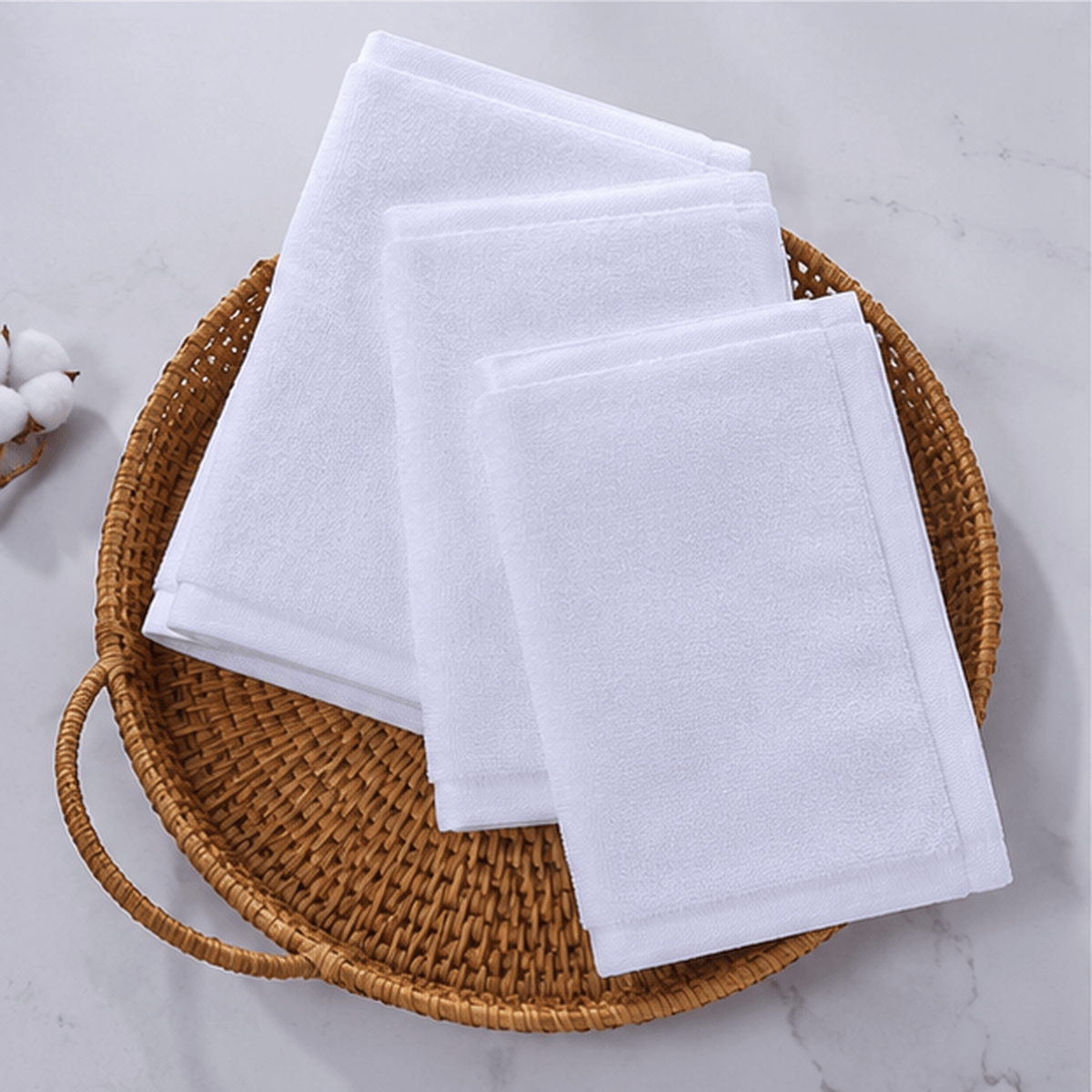 Aarniva jacquard cotton hotel face towels stacked on a woven basket, showcasing their soft texture and classic white color.